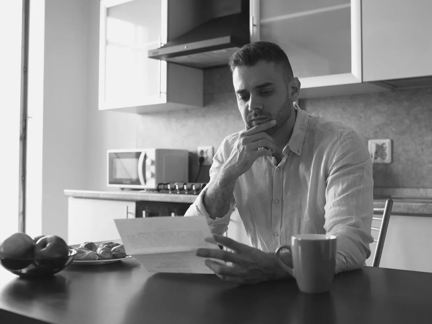 Homem relendo um documento do banco na mesa da cozinha
